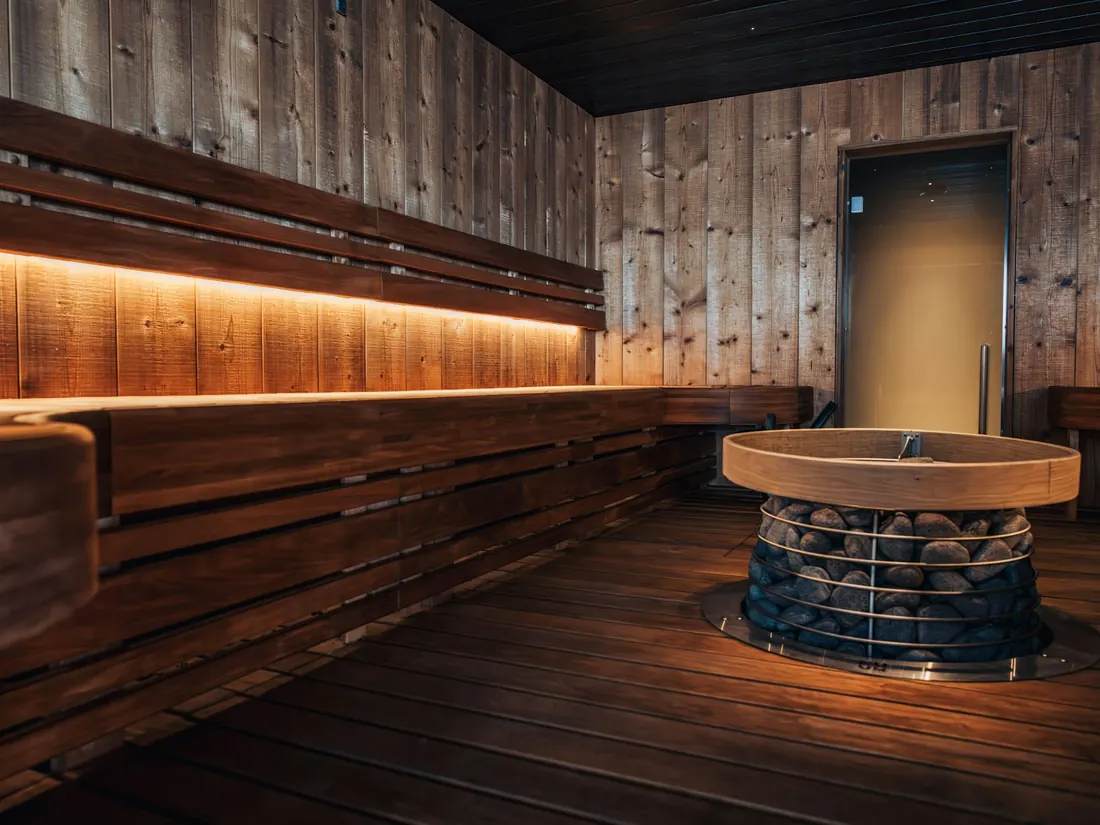 A long timber sauna bench lit from beneath, with a round stone heater